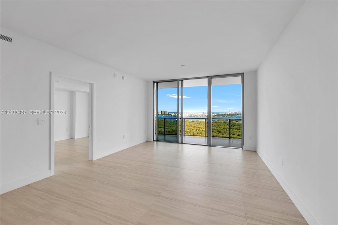 Living area featuring floor-to-ceiling sliding glass doors, neutral tile flooring, and a private balcony with water scenery