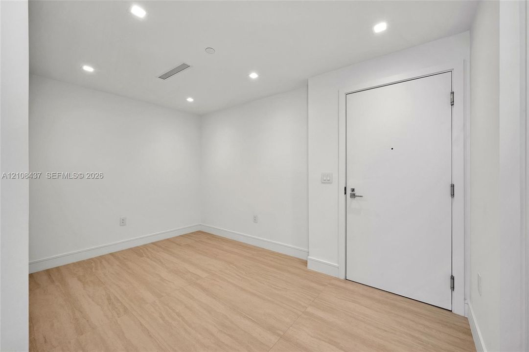 Neutral-toned room featuring wood-finish flooring, recessed lighting, and a solid-core entry door with metallic hardware