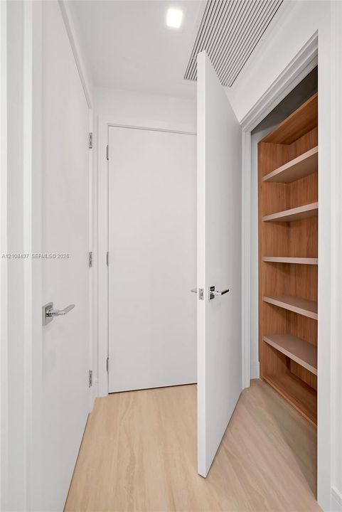 Interior corridor featuring wood-finish flooring, smooth-panel doors with satin nickel hardware, and built-in wood-finish shelving