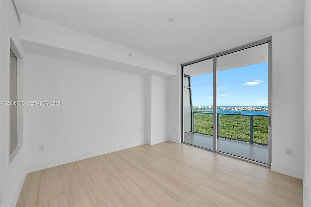 Interior space featuring wood-finish flooring, floor-to-ceiling sliding glass doors, and a private balcony with metallic railing overlooking coastal scenery