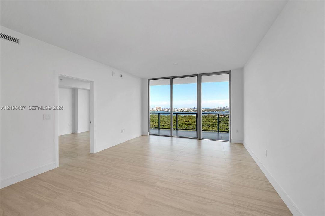 Open interior space featuring light-toned wood-finish flooring, floor-to-ceiling sliding glass doors, and a balcony with a metal railing