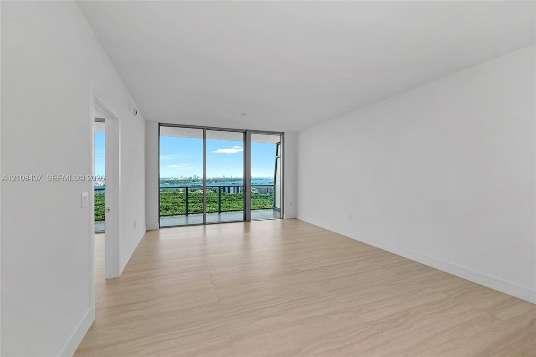 Open-concept interior featuring light-toned wood-finish flooring, floor-to-ceiling glass sliding doors, and a private balcony with a metal railing