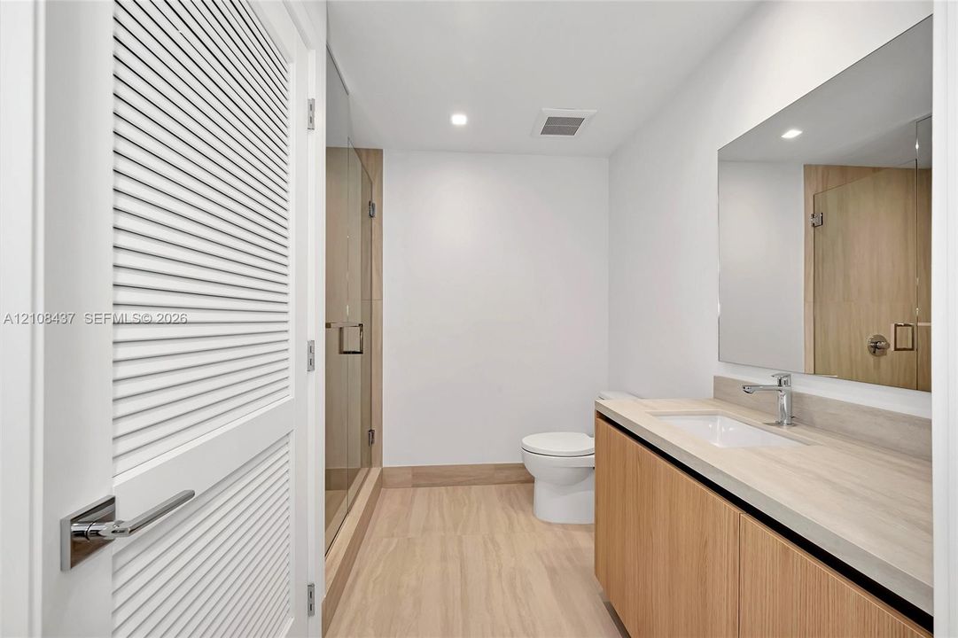 Bathroom featuring a floating vanity with wood-finish cabinetry, a large wall-mounted mirror, a glass-enclosed shower, and wood-finish flooring