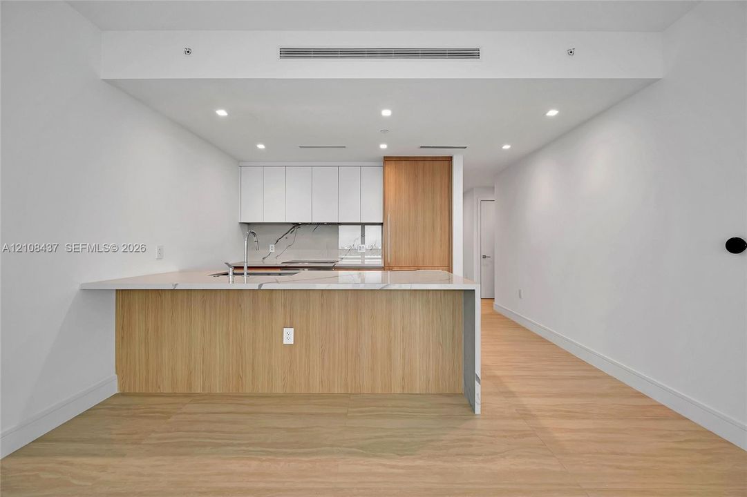 Kitchen featuring a stone-top island with waterfall edge, flat-panel cabinetry, wood-finish flooring, recessed lighting, and integrated panel-ready appliances