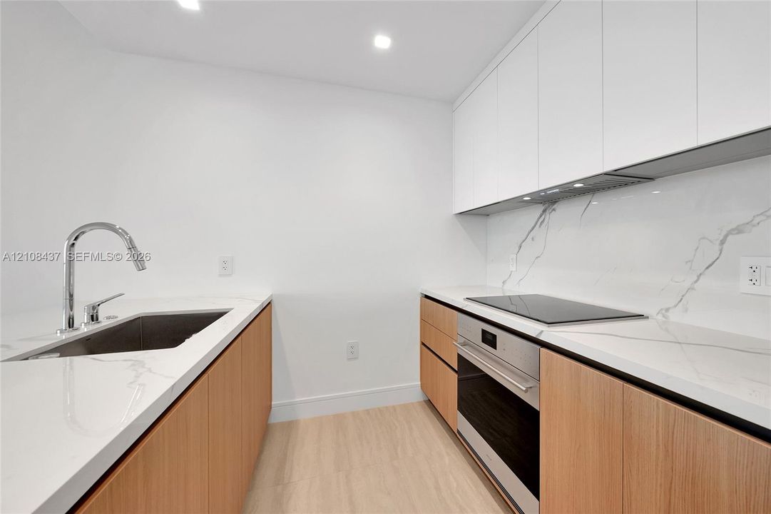 Kitchen featuring light wood-finish cabinetry, white stone countertops with integrated backsplash, stainless steel oven, electric cooktop, and undermount sink with a gooseneck faucet
