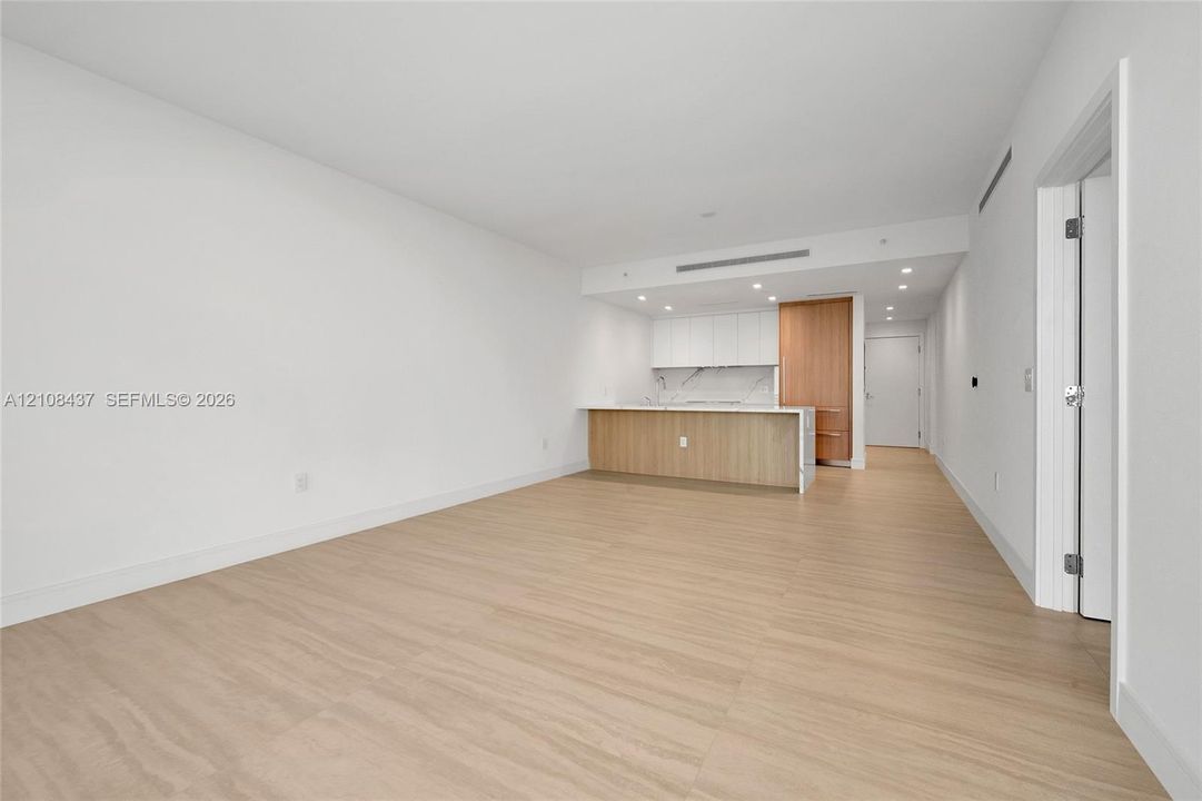 Open-concept interior featuring wood-finish flooring, recessed lighting, and a kitchen equipped with white cabinetry, wood-tone paneling, and stone-surfaced countertops