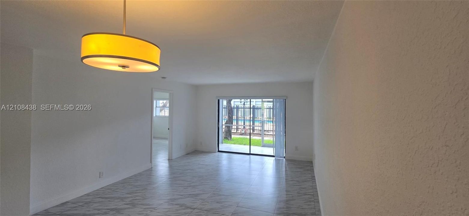 Neutral-toned tile flooring, suspended drum pendant light fixture, and sliding glass doors with exterior access