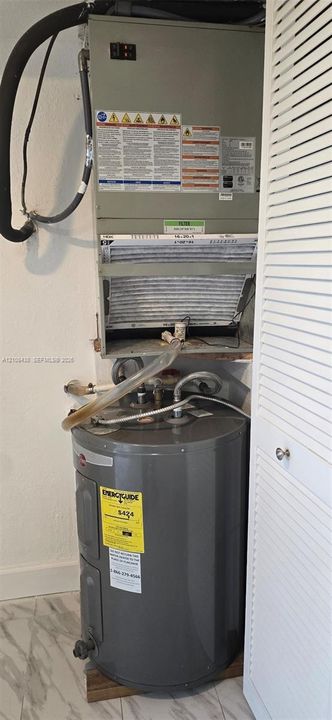 Vertical HVAC air handler unit paired with a gray cylindrical water heater, featuring louvered bi-fold closet doors and stone-finish flooring