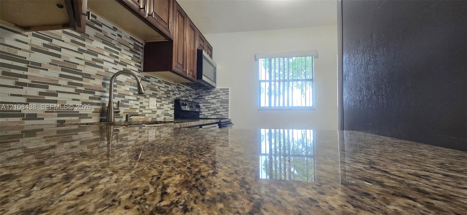 Kitchen featuring stone-finish countertops, multi-toned linear tile backsplash, dark wood-finish cabinetry, built-in microwave, and arched faucet