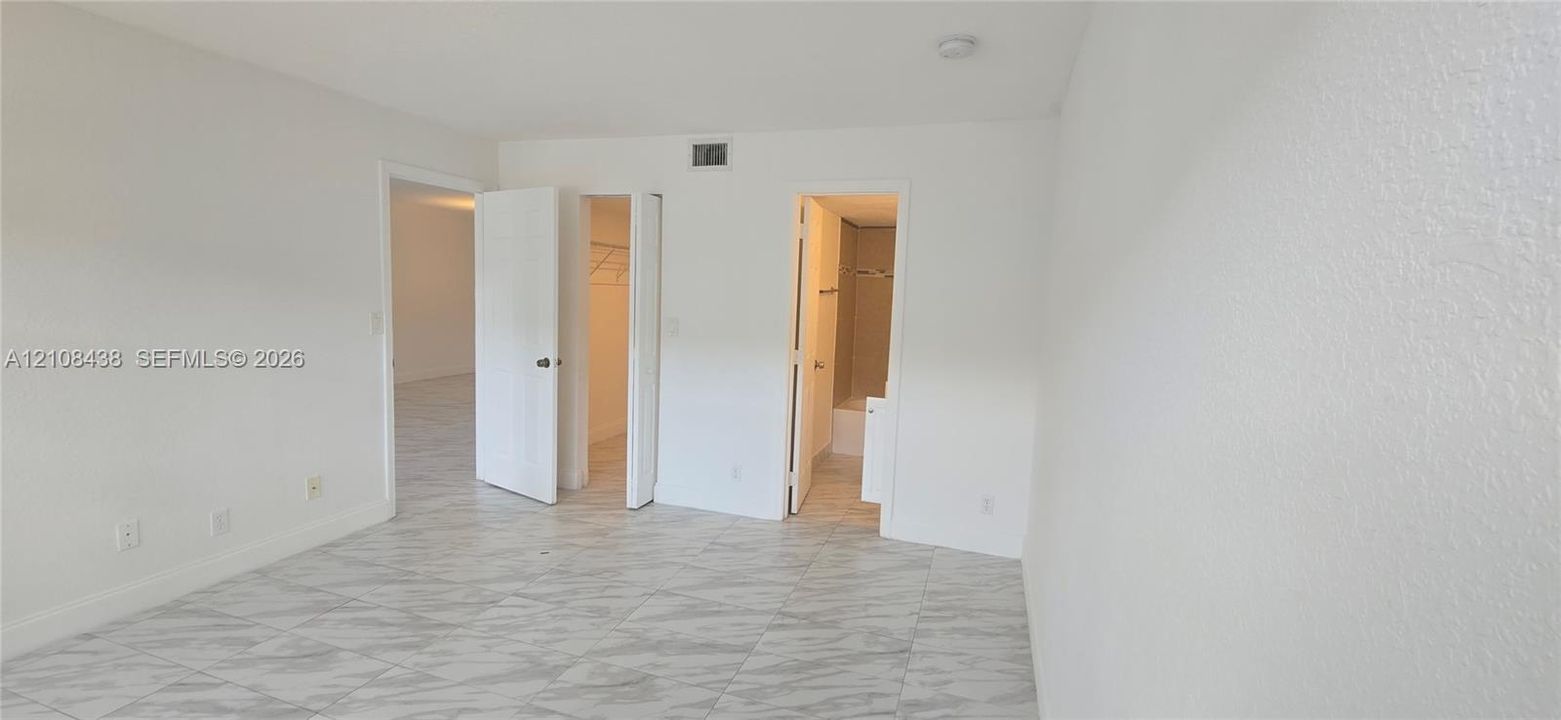 Interior space featuring large-format tile flooring with a neutral veined pattern, multiple closet entries, and a ceiling-mounted light fixture