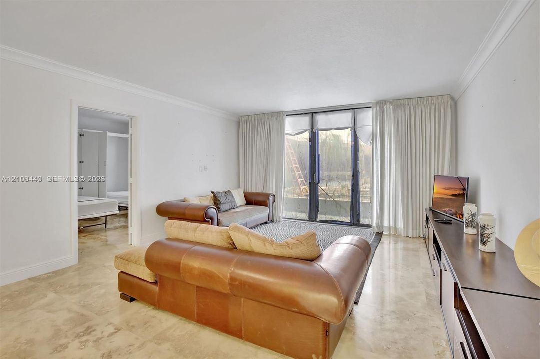 Living space featuring polished stone flooring, crown molding, and floor-to-ceiling glass sliding doors