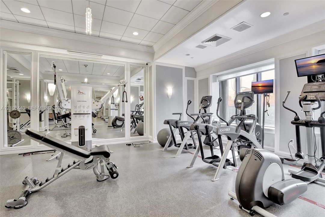 Fitness space featuring floor-to-ceiling mirrors, a coffered ceiling with recessed lighting, wall-mounted sconces, and impact-resistant rubber flooring