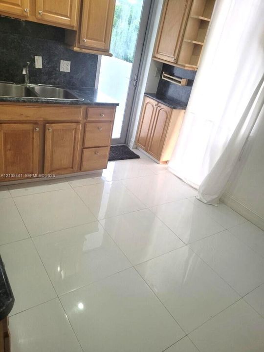 Kitchen featuring wood cabinetry, dark stone-finish countertops, dual-basin stainless steel sink, and polished white tile flooring