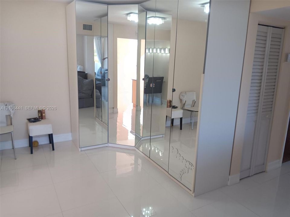 Floor-to-ceiling mirrored wardrobe featuring integrated cabinetry, reflective finish, and white tile flooring throughout, accented by louvered-panel closet doors and recessed lighting