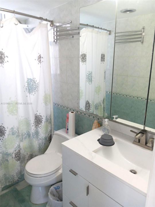 Bathroom featuring a white vanity cabinet with an integrated rectangular sink, a stone-finish countertop, a wall-mounted mirrored medicine cabinet, and tiled walls with decorative trim