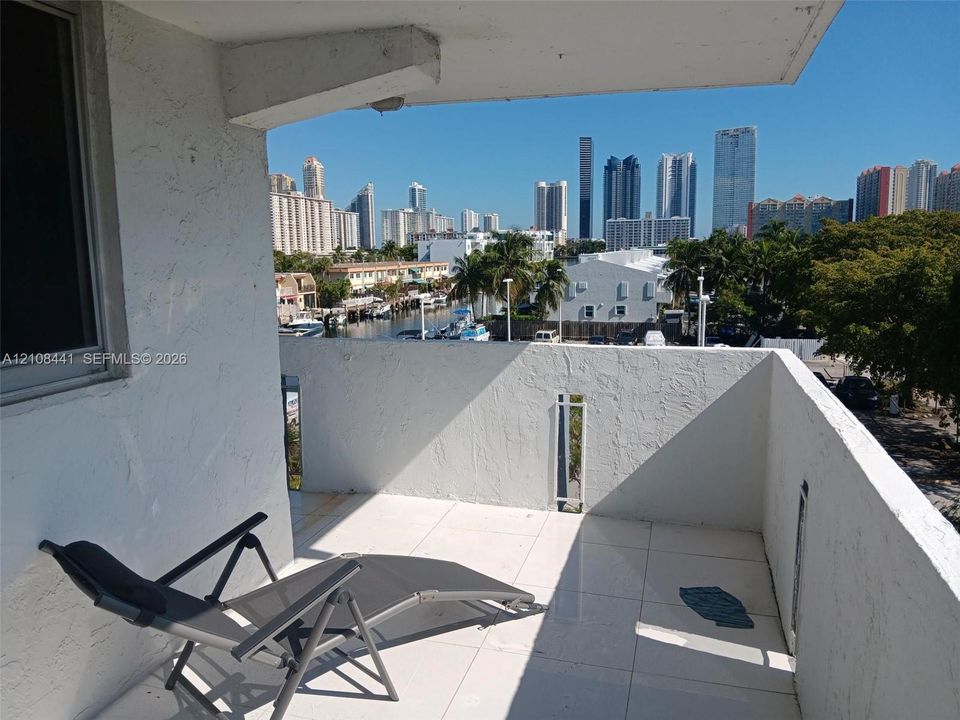 Private balcony featuring white tiled flooring, stucco walls, and an urban skyline backdrop