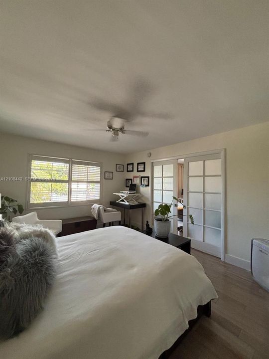 Wood-finish flooring, white-framed multi-pane sliding doors, white plantation shutters, and a ceiling fan