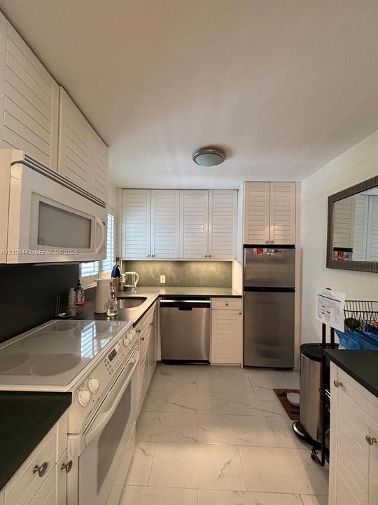 Kitchen featuring white louvered cabinetry, stainless steel appliances, dark countertops, and light-toned tile flooring