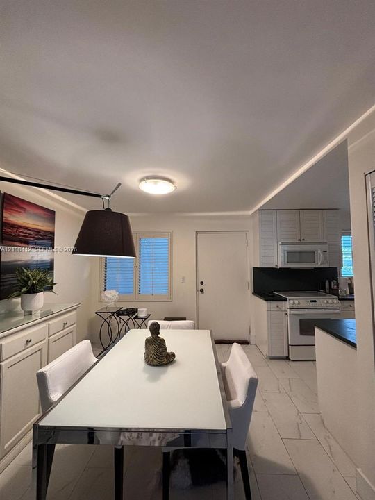 Kitchen and dining area featuring stone-look tile flooring, white cabinetry with louvered-style doors, matte black countertops, and a built-in over-the-range microwave