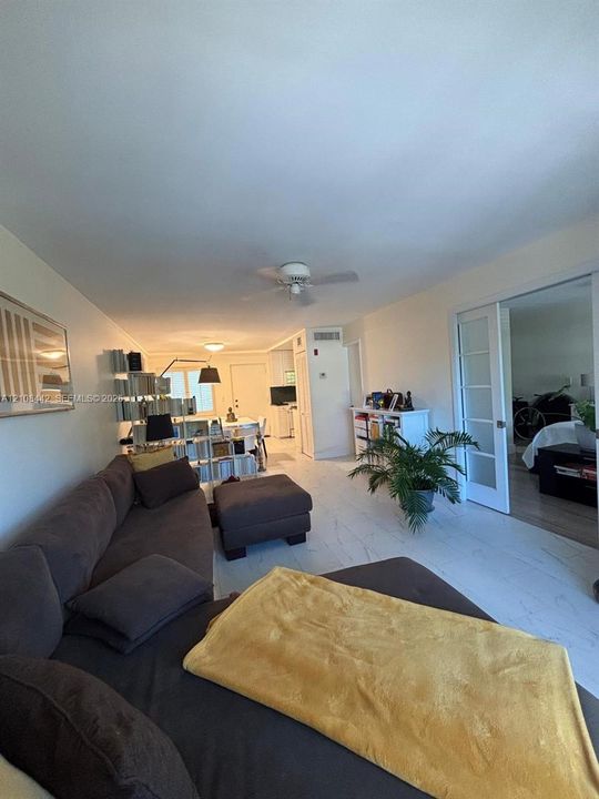 Large-format light-toned tile flooring throughout the main living area, white French doors, and ceiling-mounted fans