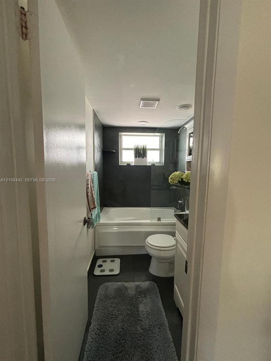 Bathroom featuring a deep soaking tub, dark tiled walls, glass shower panel, and white vanity cabinetry with a dark countertop