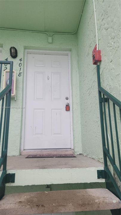 Exterior entry featuring a white six-panel door, textured stucco siding, concrete stairs, and metal railings