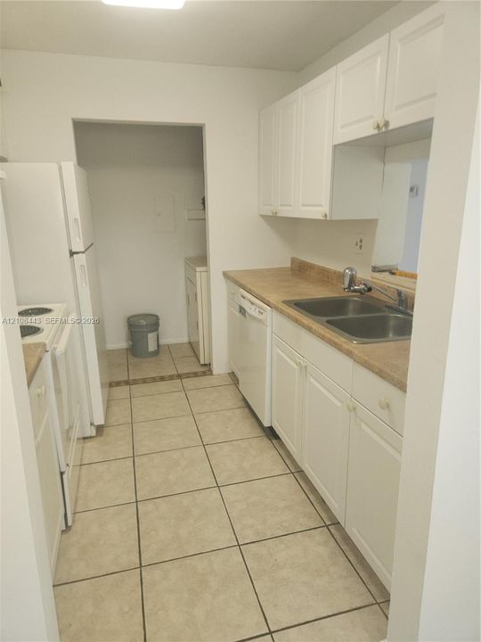 Kitchen featuring white cabinetry, solid-surface countertops, dual-basin stainless steel sink, built-in dishwasher, and ceramic tile flooring