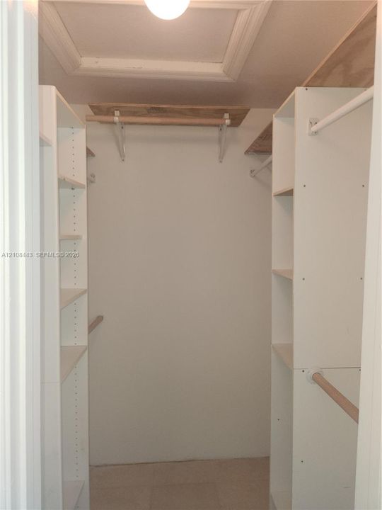 Storage space featuring white built-in shelving towers, wooden hanging rods, and upper wood-finish shelving