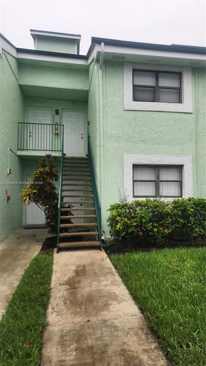 Two-story exterior featuring a textured stucco finish, white window trim, a metal staircase with railings, and a concrete walkway