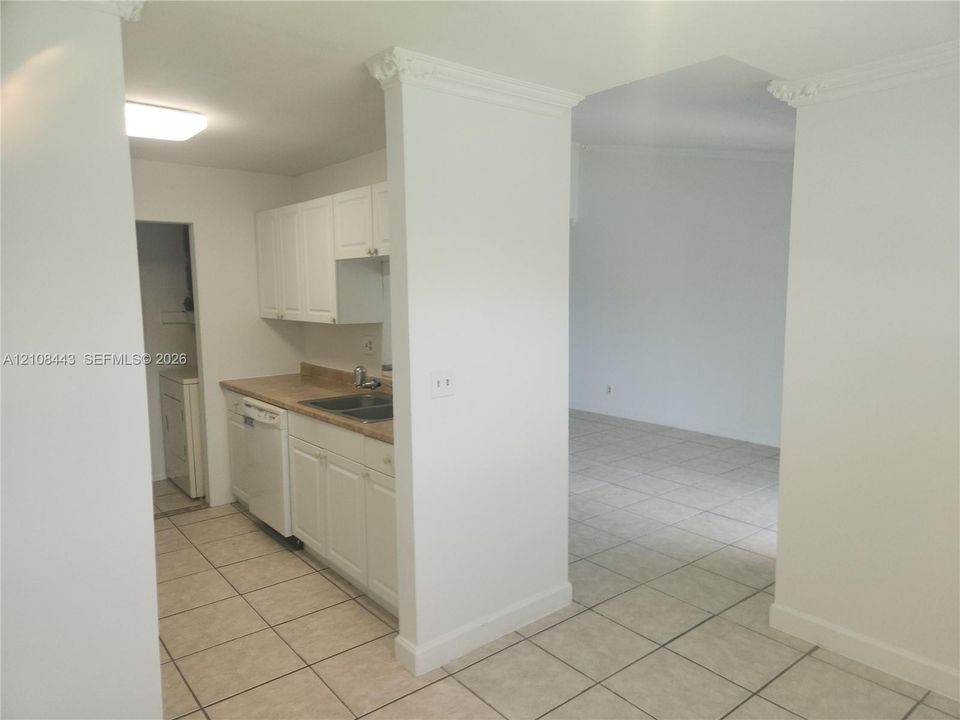 Kitchen featuring white cabinetry, solid-surface countertops, dual-basin stainless steel sink, built-in dishwasher, and ceramic tile flooring throughout