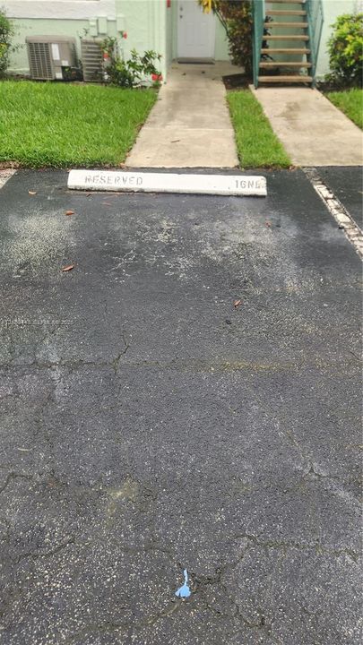 Designated parking space with concrete bumper, asphalt surface, and concrete walkway