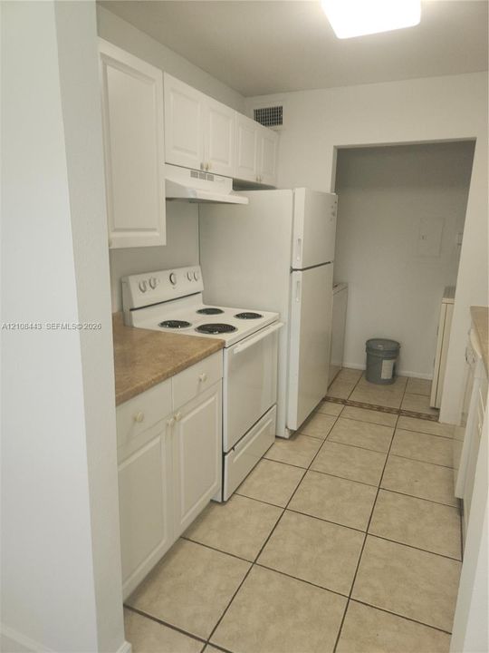 Kitchen featuring white cabinetry, solid-surface countertops, tile flooring, and integrated white appliances