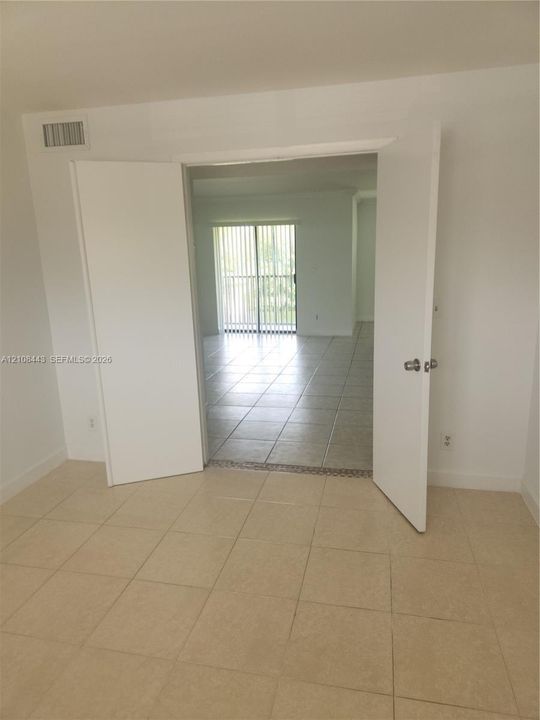 Interior space featuring light-toned ceramic tile flooring, white-painted double doors, and sliding glass balcony doors