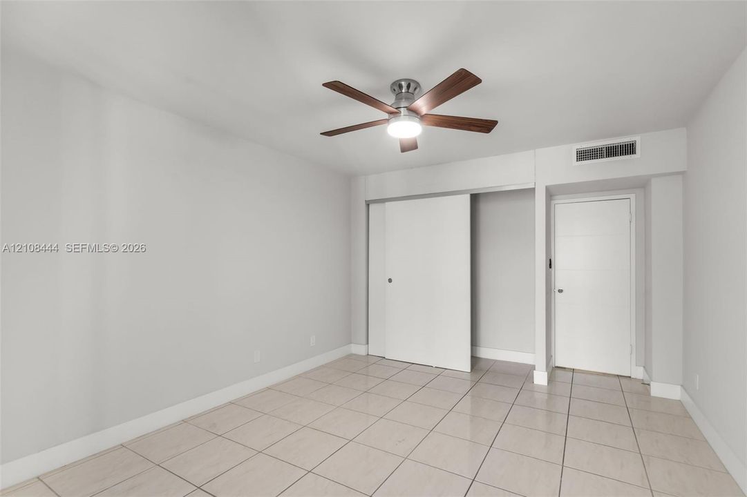 Neutral-toned room featuring large-format tile flooring, a multi-blade ceiling fan with integrated lighting, a sliding-door closet, and a contemporary flat-panel door