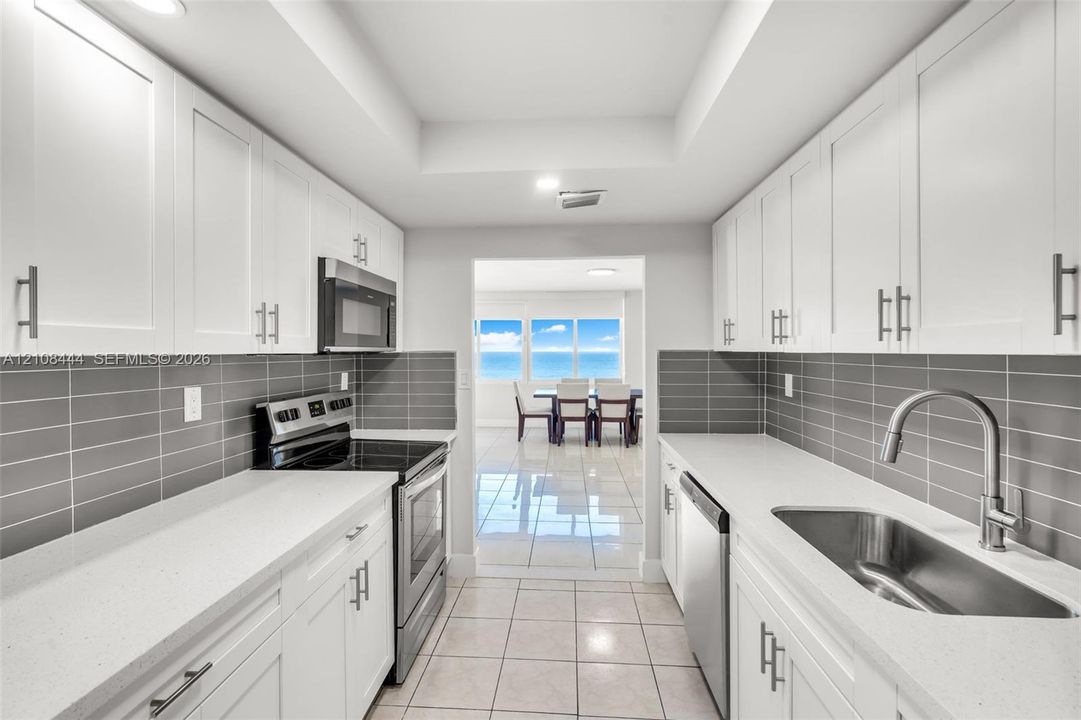 Kitchen featuring white shaker-style cabinetry, solid-surface countertops, horizontal gray tile backsplash, stainless steel appliances, and large-format tile flooring