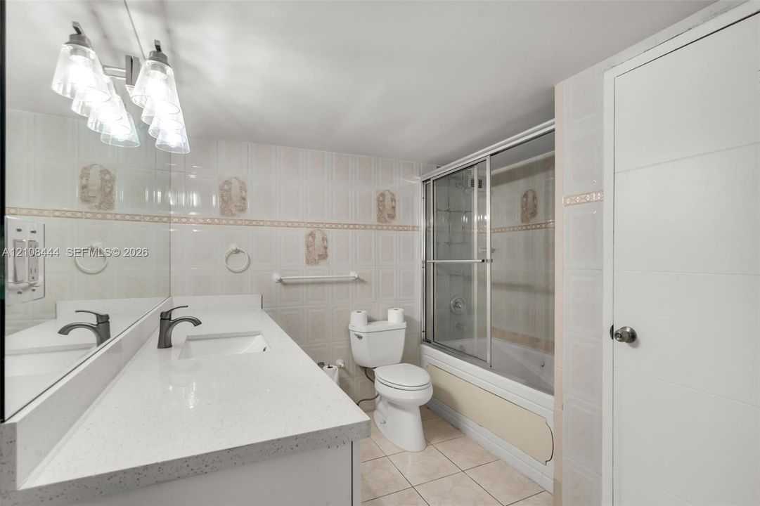 Bathroom featuring a quartz-topped vanity with an integrated basin, ceramic tile flooring, full-width wall mirror, and a tub-shower combination enclosed by sliding glass doors