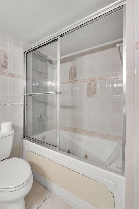 Jetted soaking tub with integrated shower, sliding glass enclosure, and wall-mounted plumbing fixtures surrounded by ceramic tile wall accents