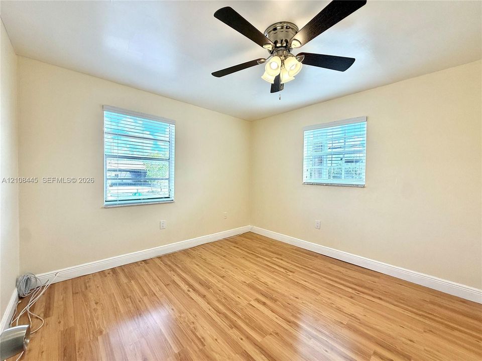 Bedroom 2 featuring wood-finish flooring, two windows with horizontal blinds, and a central ceiling fan with multi-light fixture