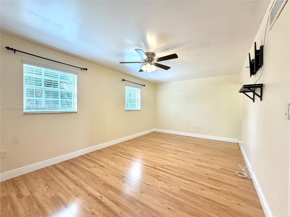 Neutral interior featuring wood-finish flooring, two dual-pane windows with metal curtain rods, and a ceiling-mounted light fixture with a fan