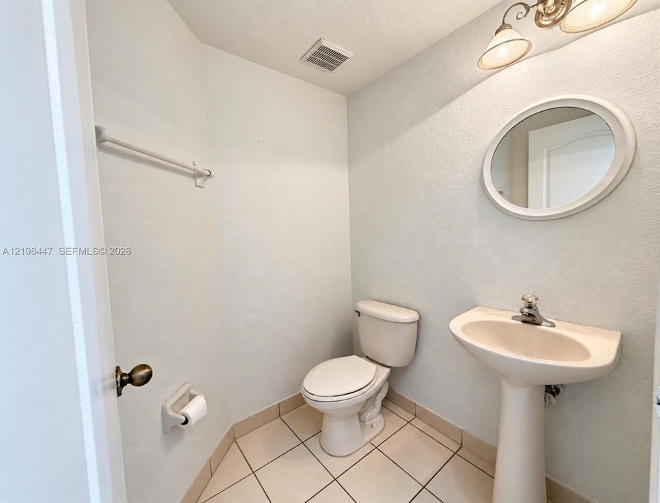 Pedestal sink with a single-handle faucet, oval wall-mounted mirror, ceramic tile flooring, and integrated lighting fixture
