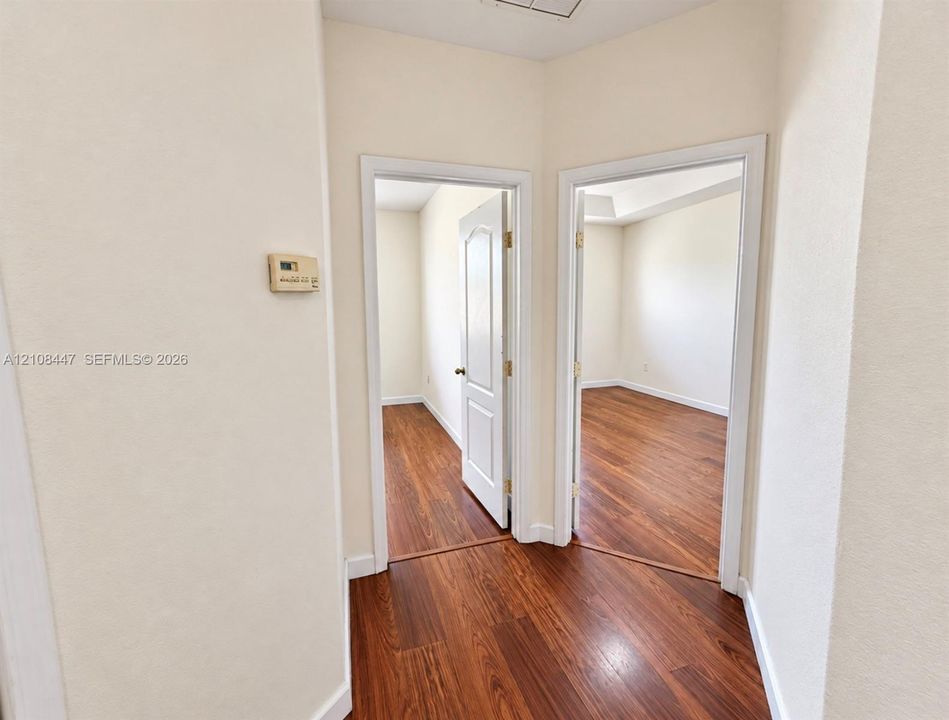 Interior hallway featuring wood-finish flooring, two sets of white casing-trimmed doorways, and interior raised-panel doors
