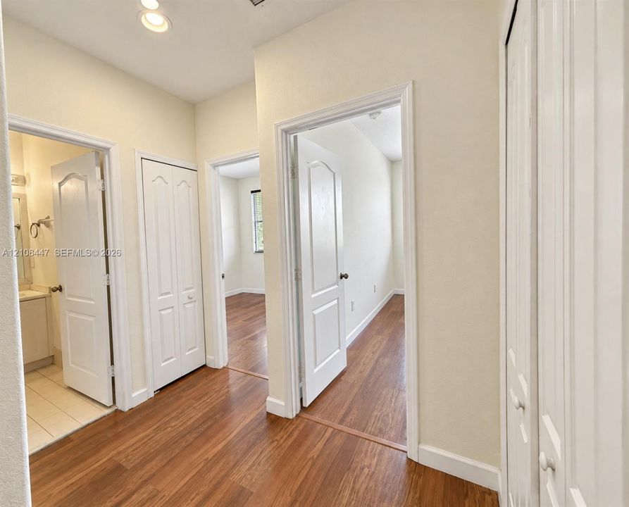Hallway featuring wood-finish flooring, white paneled interior doors, and multiple built-in closets with bi-fold doors