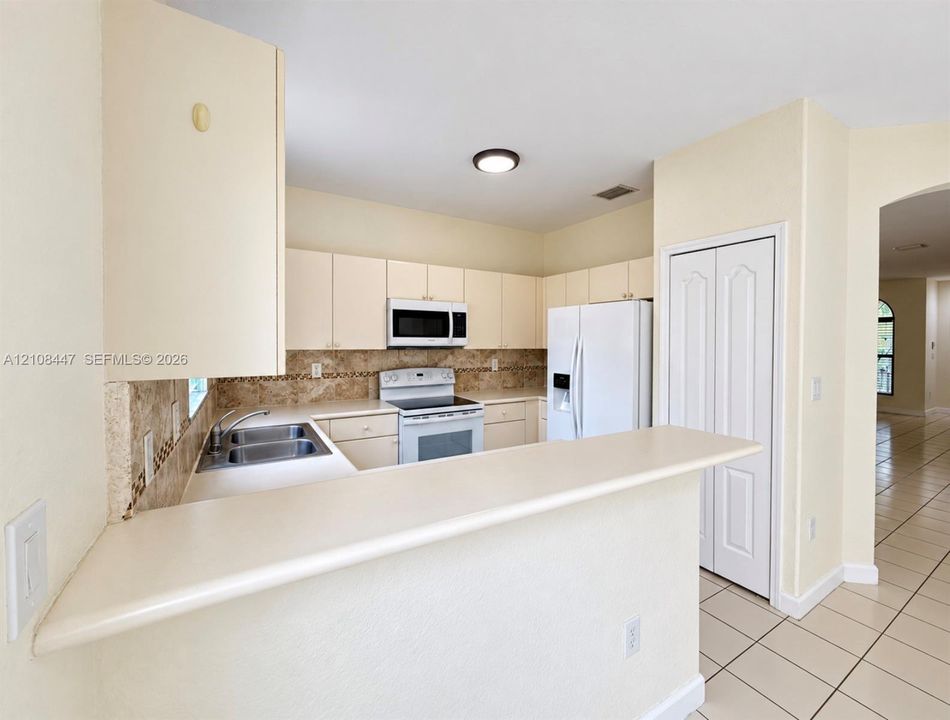 Kitchen featuring a breakfast bar, stone-pattern backsplash, white flat-panel cabinetry, and tile flooring