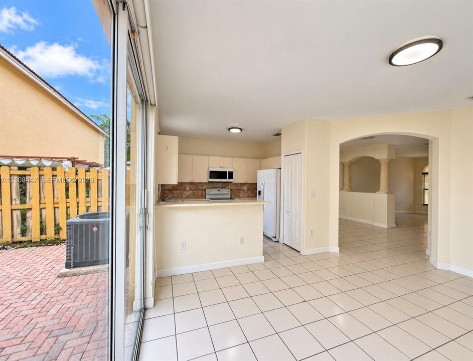 Kitchen featuring a breakfast bar, stone-finish backsplash, and built-in cabinetry, with ceramic tile flooring and sliding glass doors opening to a brick-paved patio