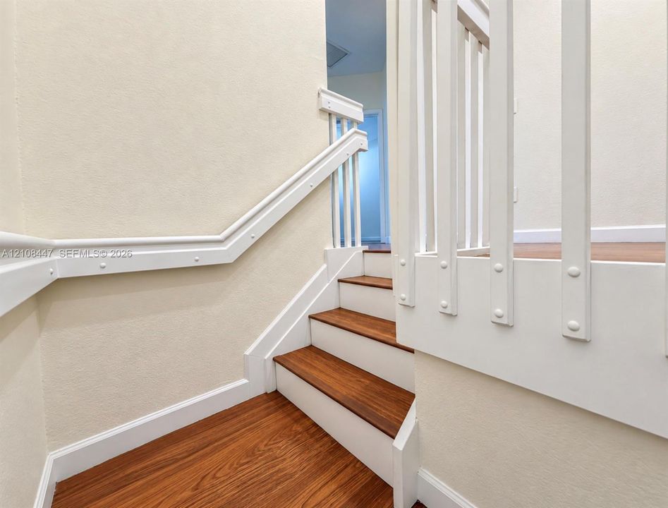 Staircase featuring wood-finish treads, white risers, a matching wood-finish handrail, and white vertical balusters
