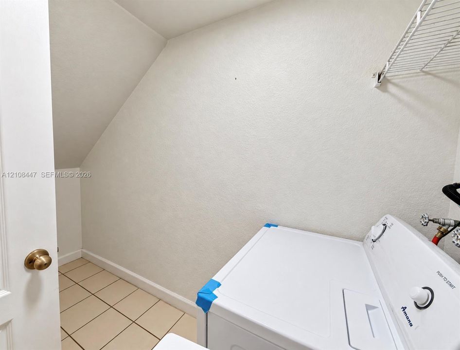 Utility space featuring neutral-toned tile flooring, white walls, and a built-in wire shelving unit