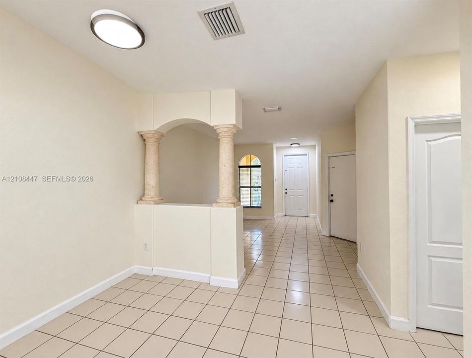 Interior space featuring decorative stone-texture columns, an arched architectural opening, ceramic tile flooring, and a multi-panel door with an arched window