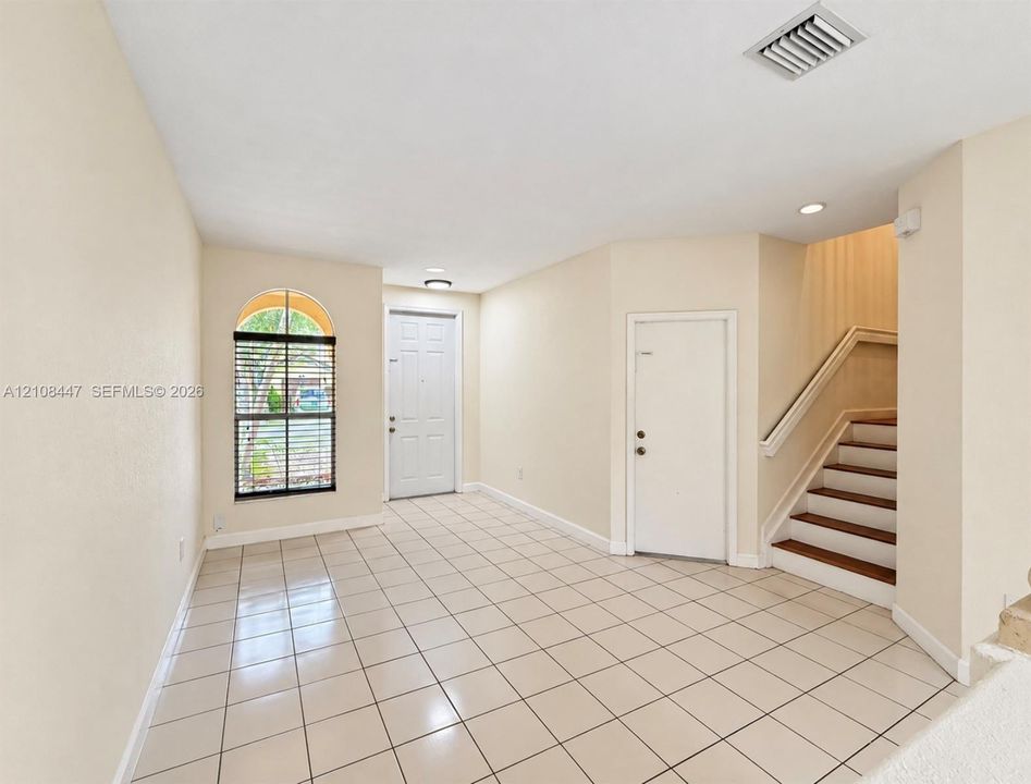 Interior entrance featuring light-toned ceramic tile flooring, arched window, recessed lighting, and a staircase with wood-finish treads and a handrail