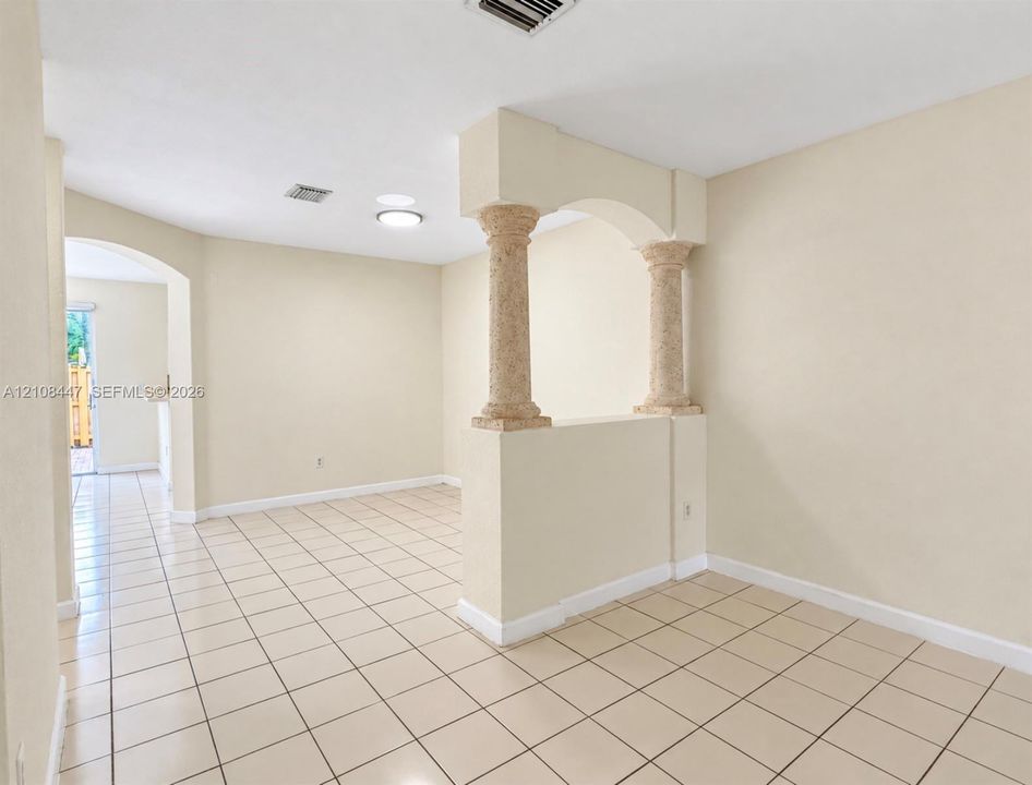 Interior space featuring neutral wall tones, ceramic tile flooring, textured stone-style pillars, and arched structural detailing