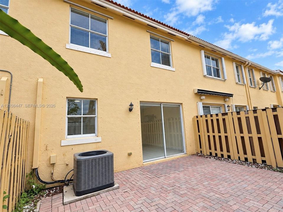 Stucco exterior featuring a brick paver patio, sliding glass door, and wooden privacy fencing